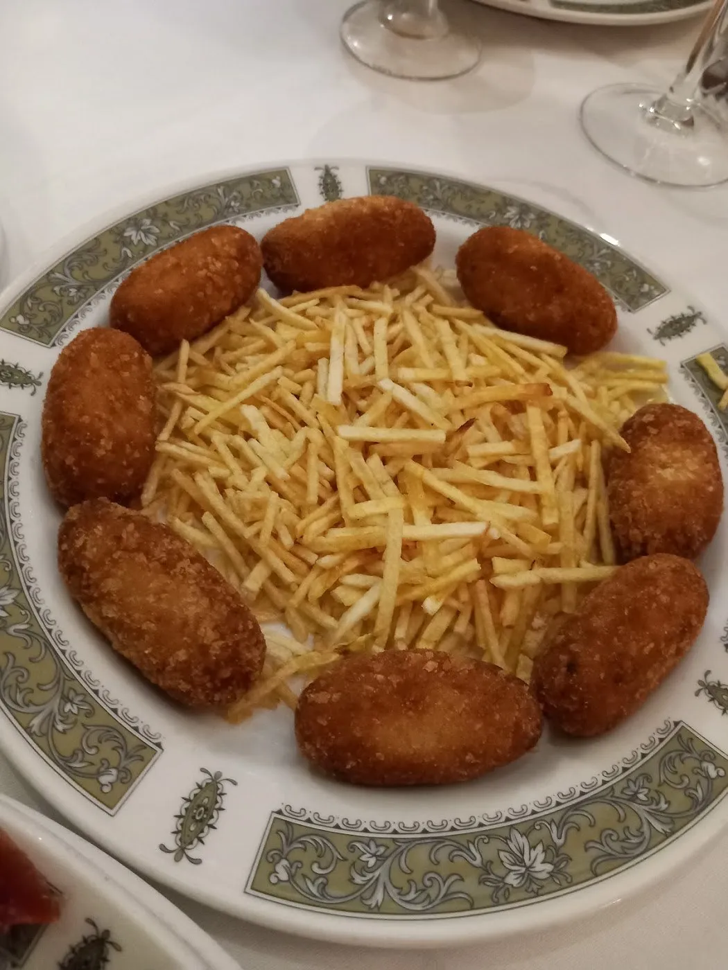 Croquetas en corona alrededor de patatas paja en plato con orla verde