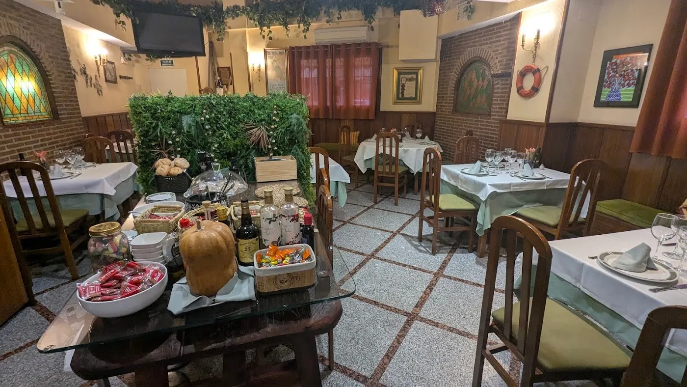 Comedor con mesas vestidas, paredes de ladrillo, vidriera y un seto de hojas al fondo