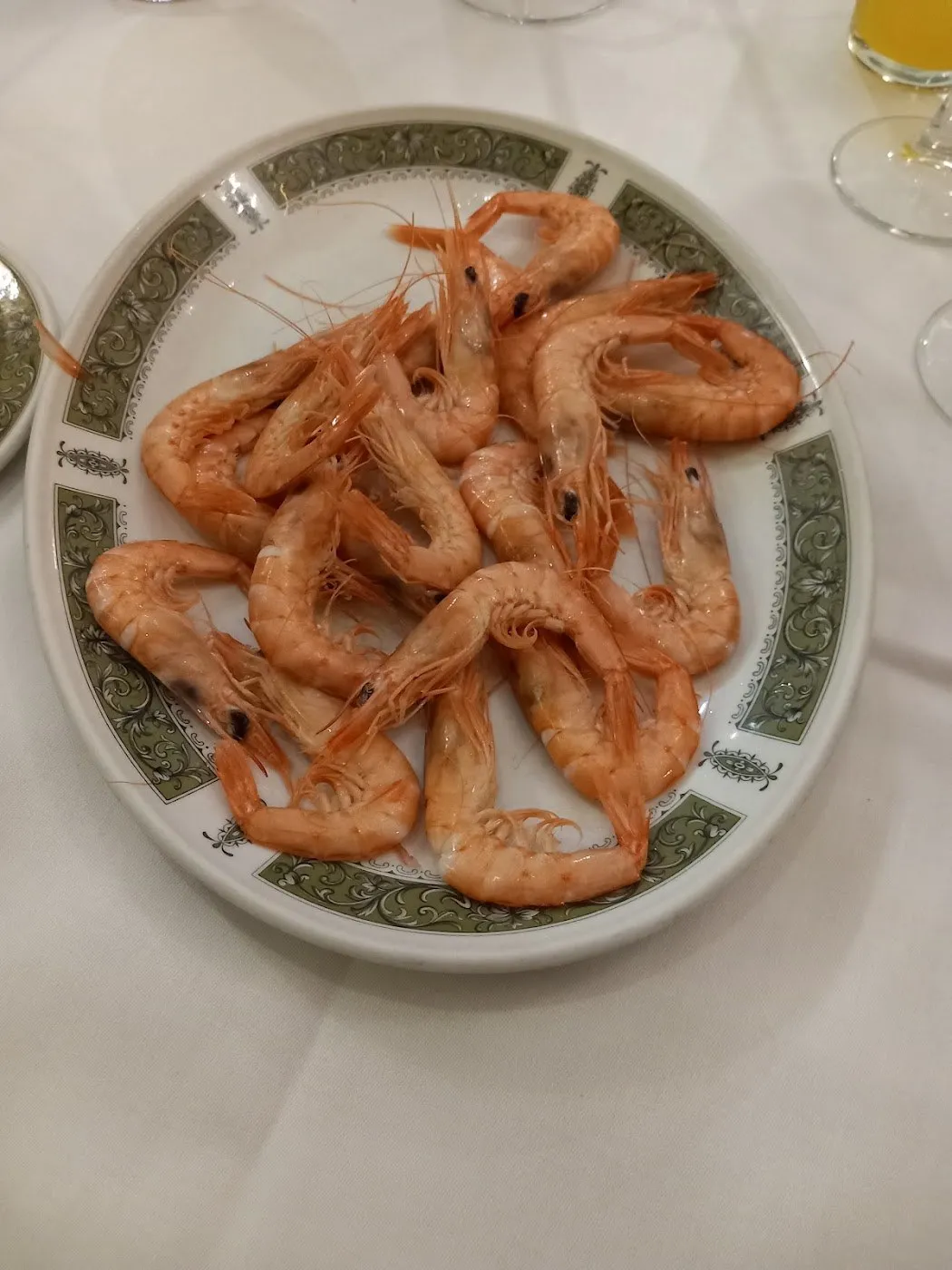 Gambas cocidas en plato con orla verde sobre mantel blanco