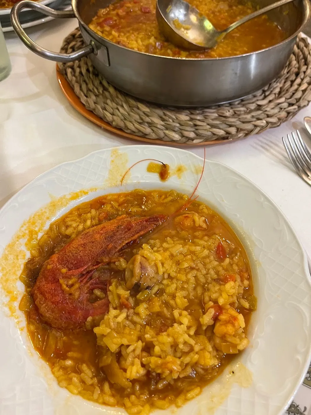 Arroz caldoso con un carabinero en plato hondo blanco y la cazuela al fondo
